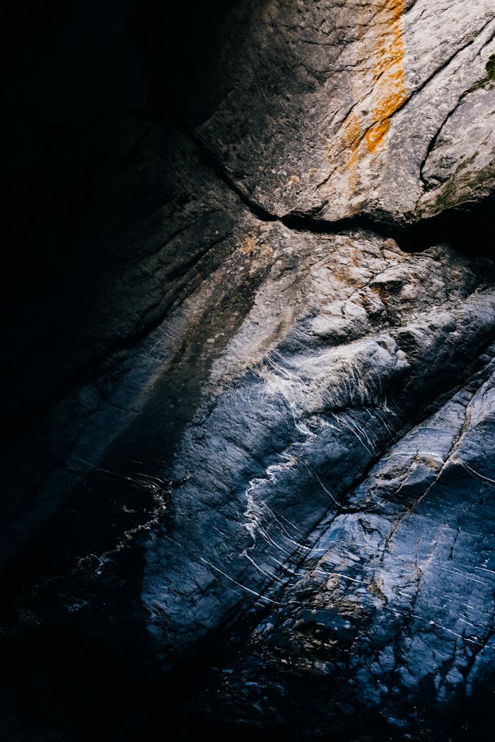 Moody vertical shot of a textured rock surface with dark tones and rough edges.